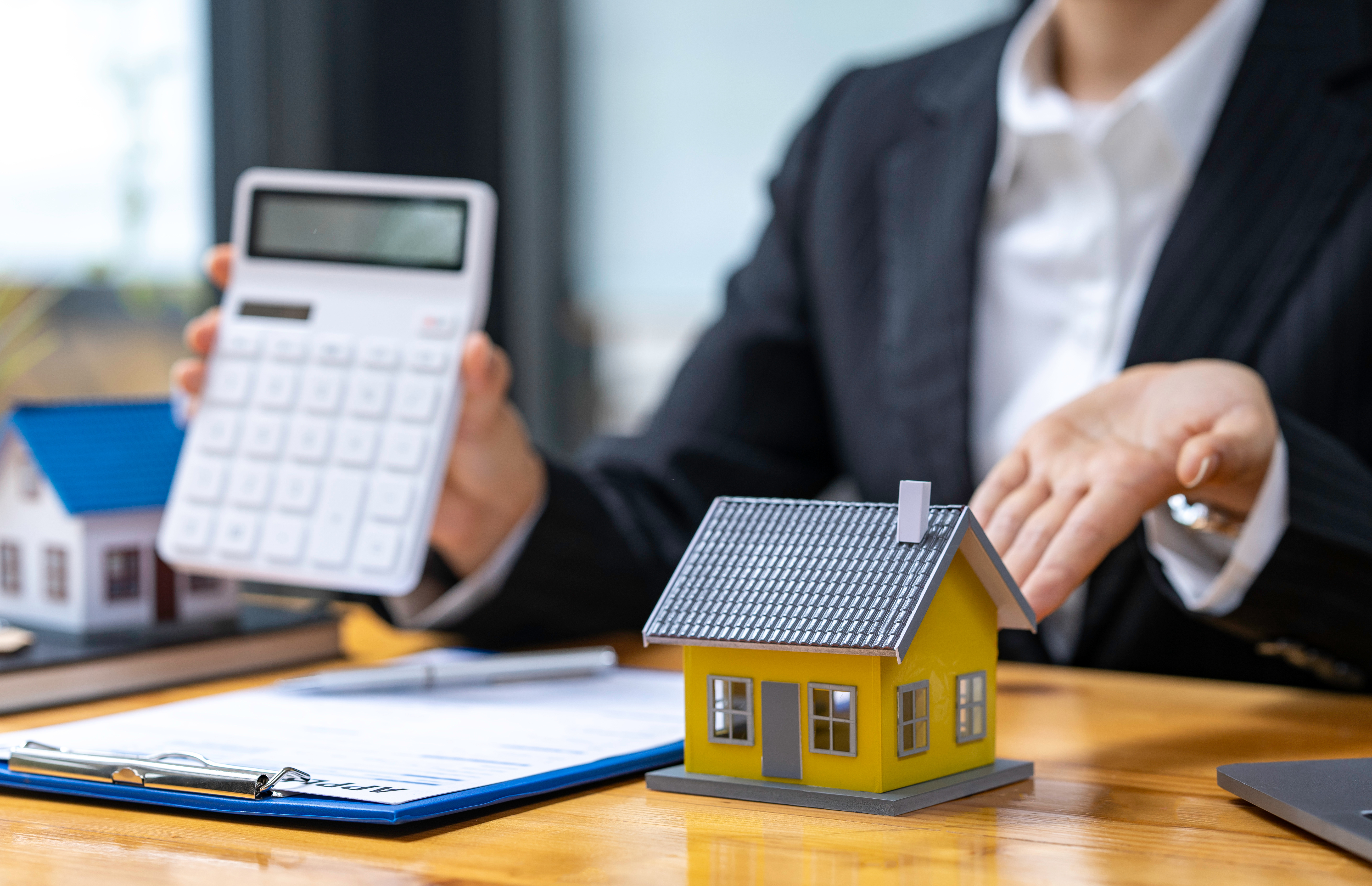 Mortgage advisor holding calculator and pointing at a house