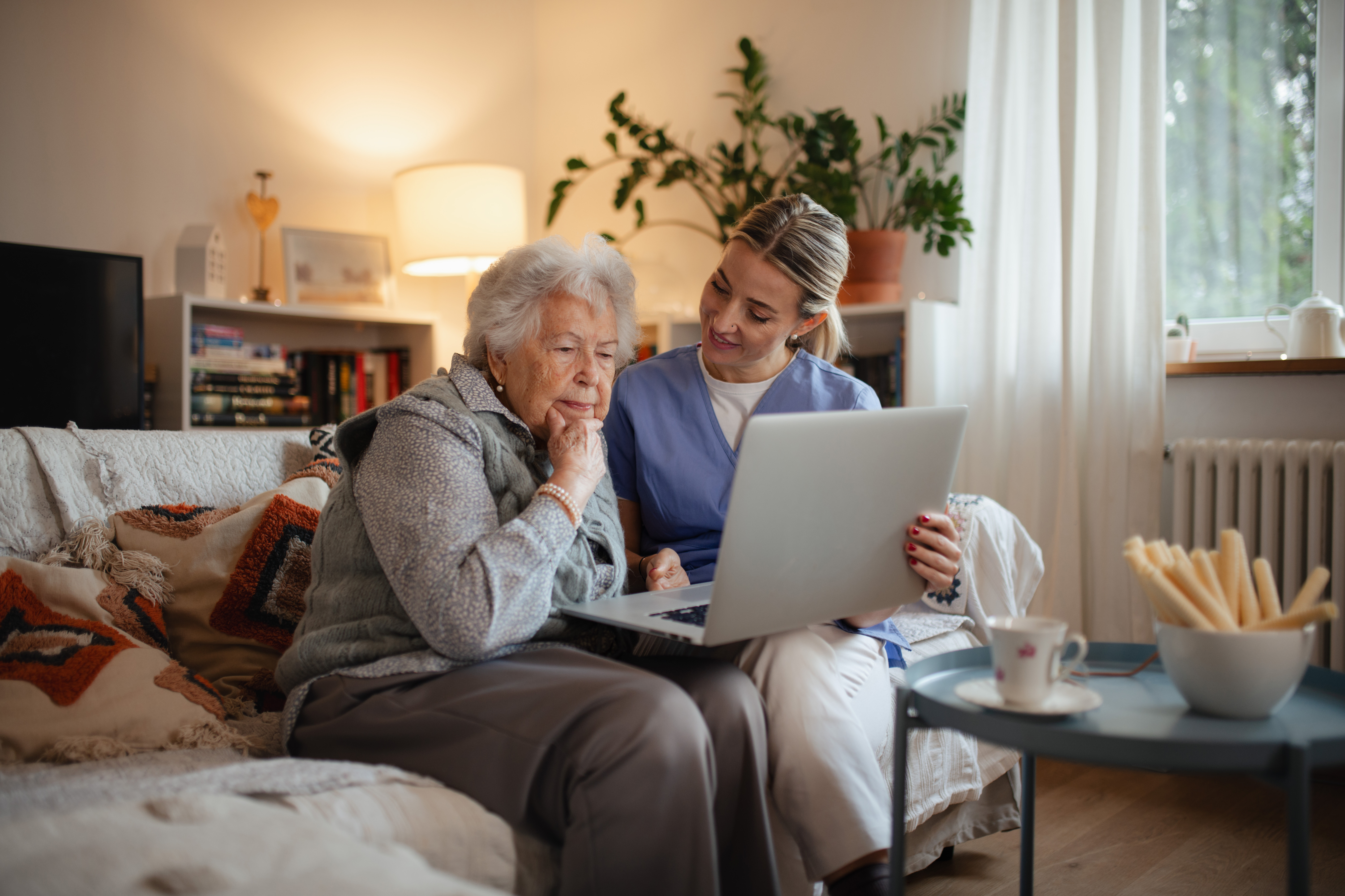 Social worker helping elderly lady with managing her finances, teaching her to use online banking on laptop.