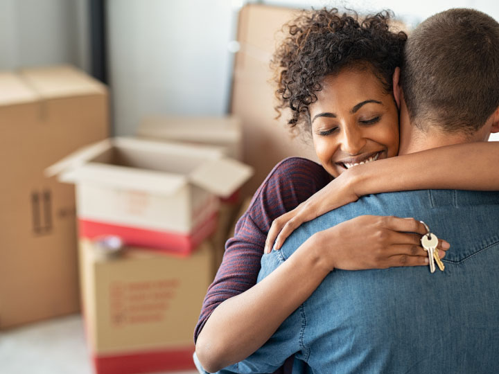 Couple embracing with house keys and boxes in new home