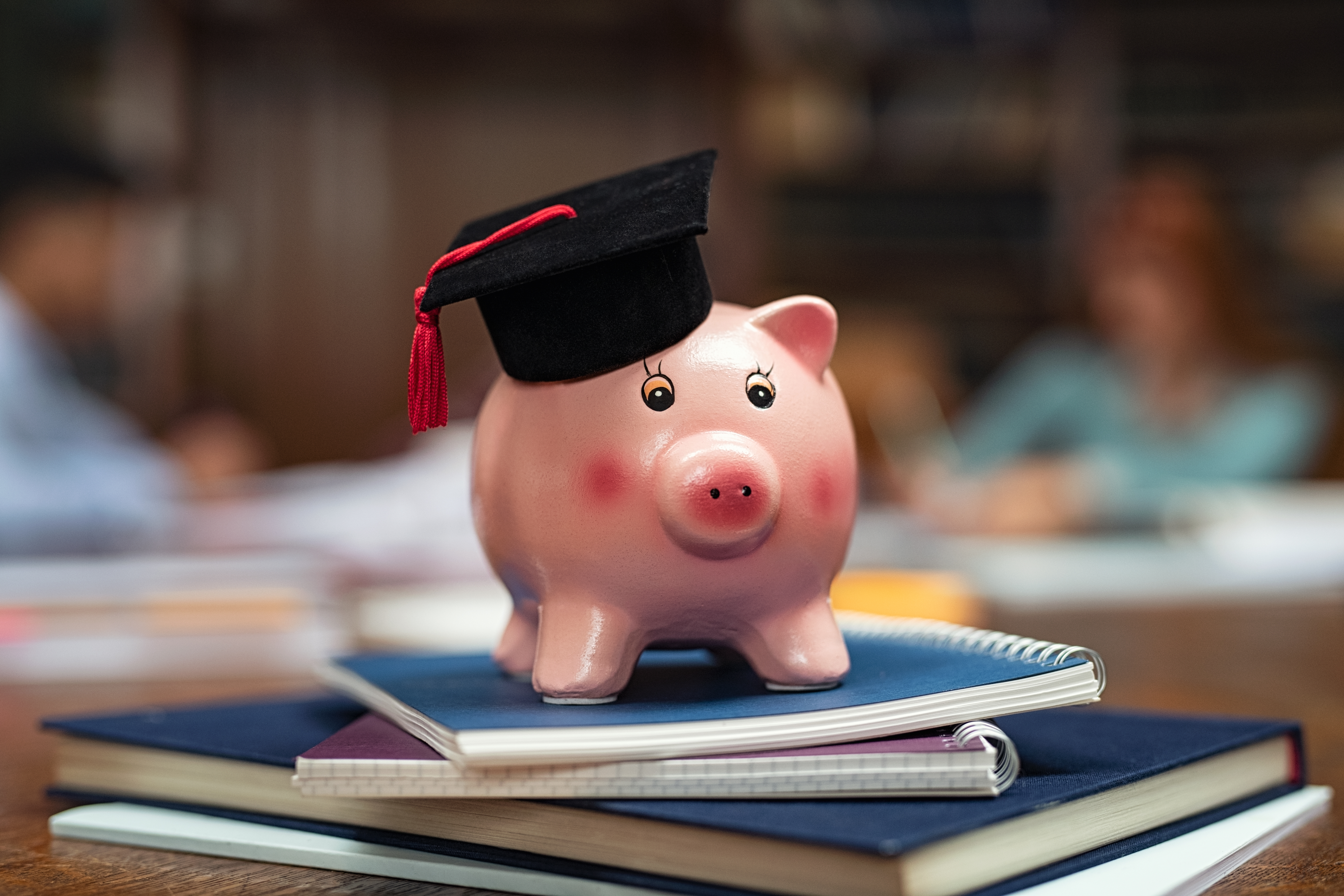 Piggy bank with graduation cap atop notebooks