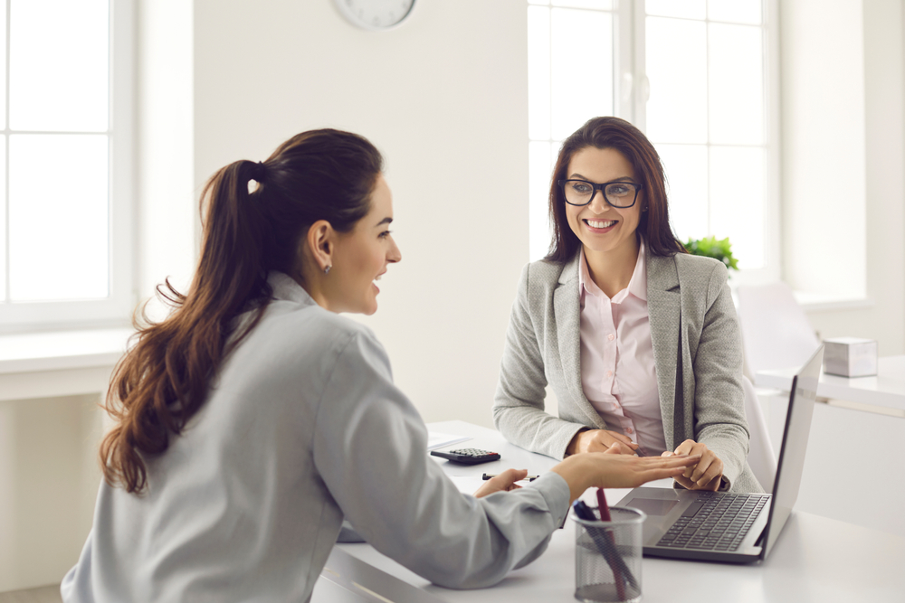 two women sitting at a table looking at a laptop