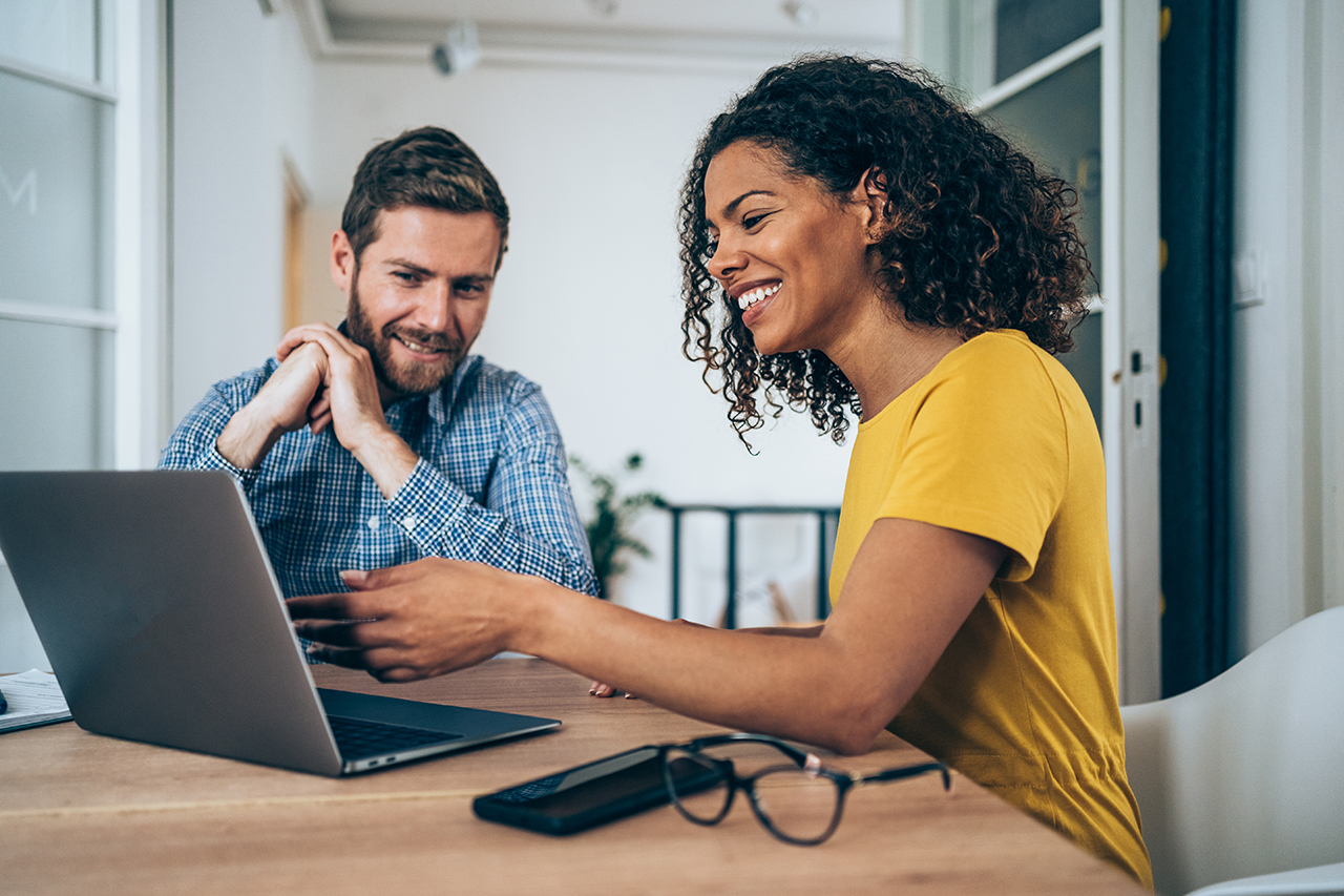 Man and woman smiling and working on a laptop at home