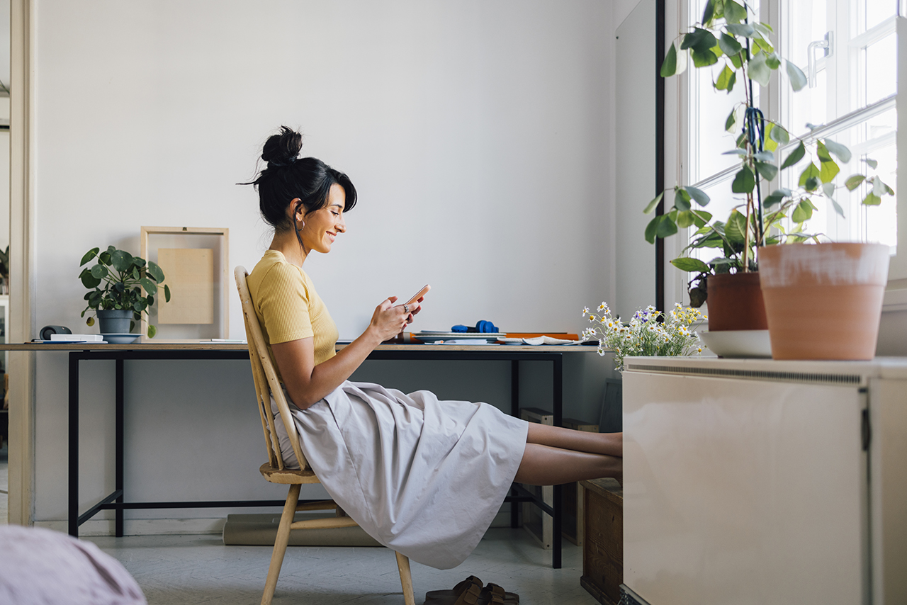 Woman sitting at a desk, using a smartphone in a cozy workspace