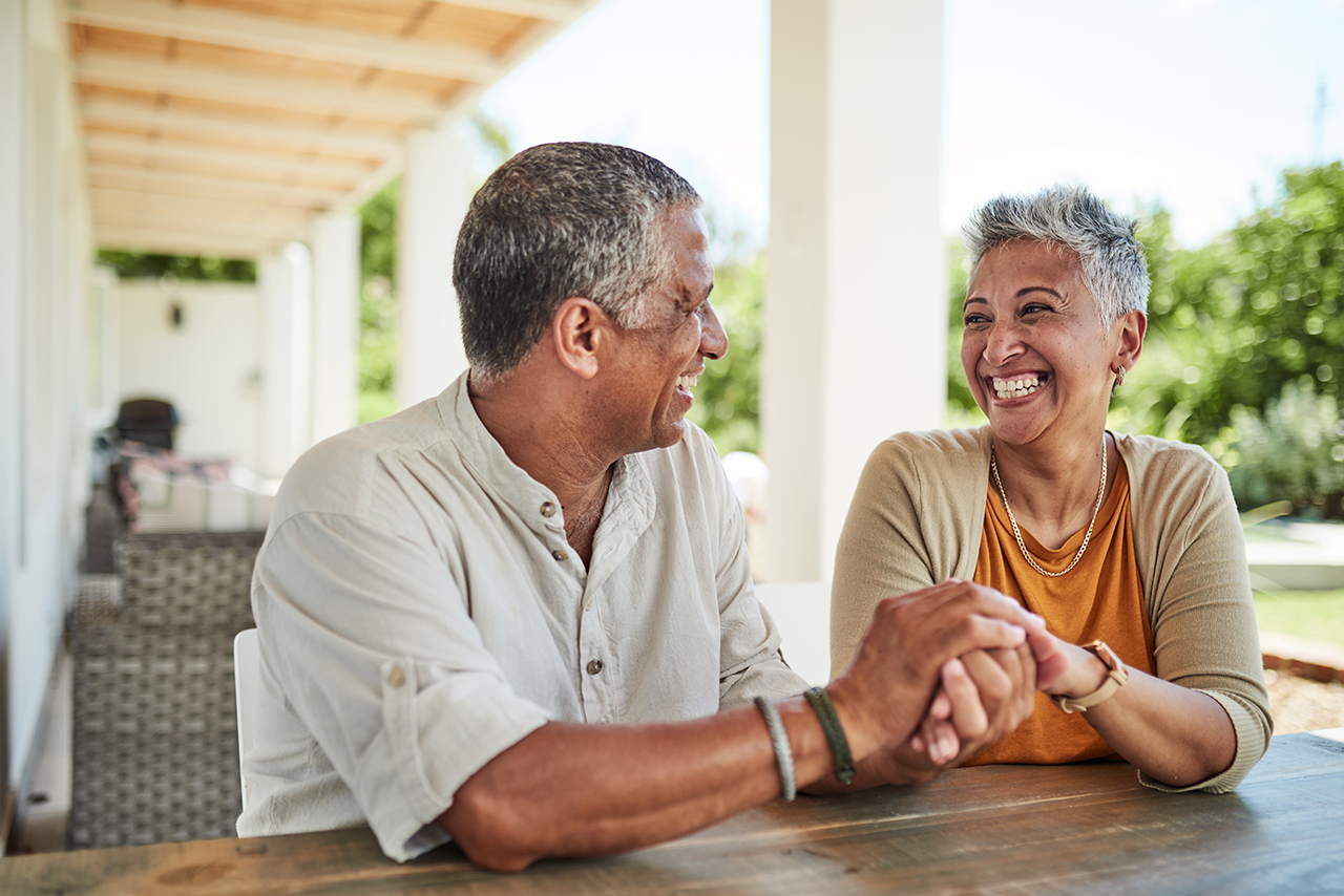 Older couple sitting at an outdoor table, holding hands and smiling
