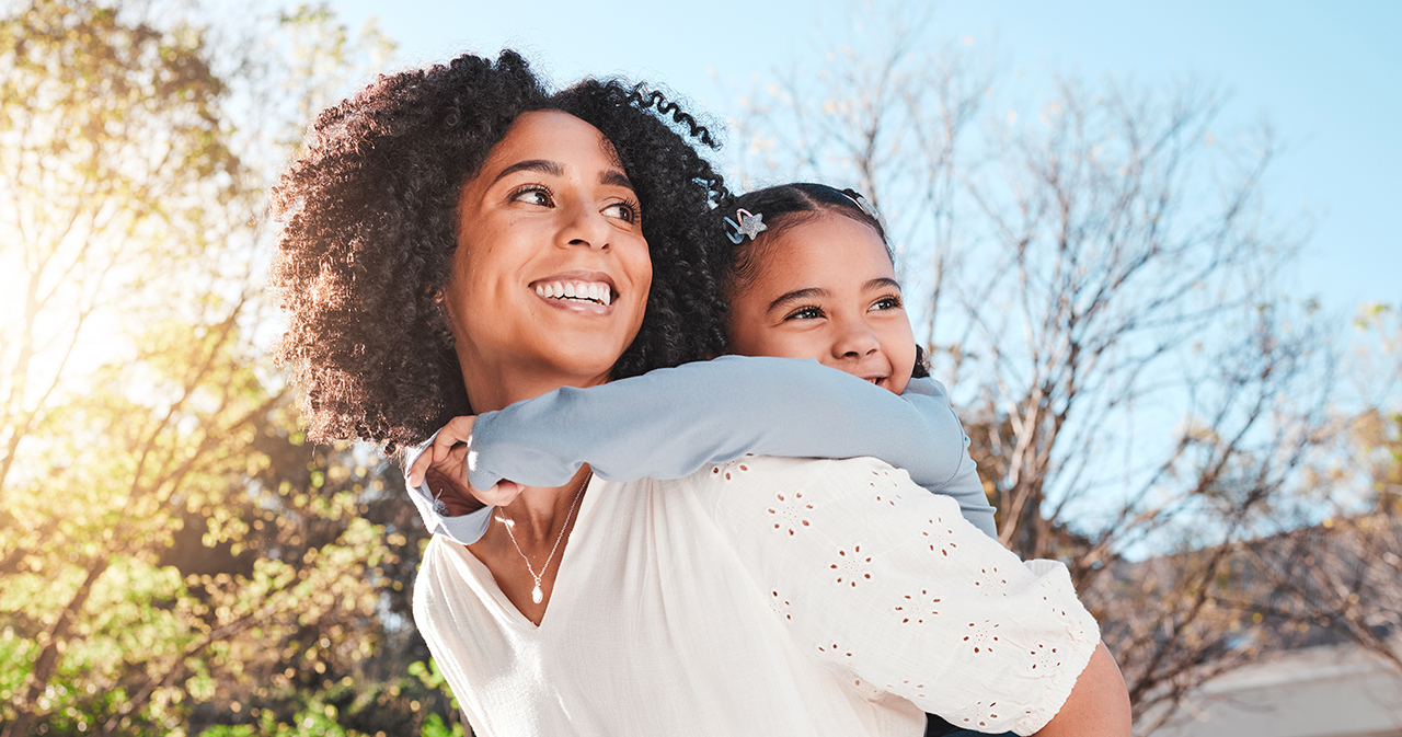 Mother hugging her young daughter outdoors, both smiling