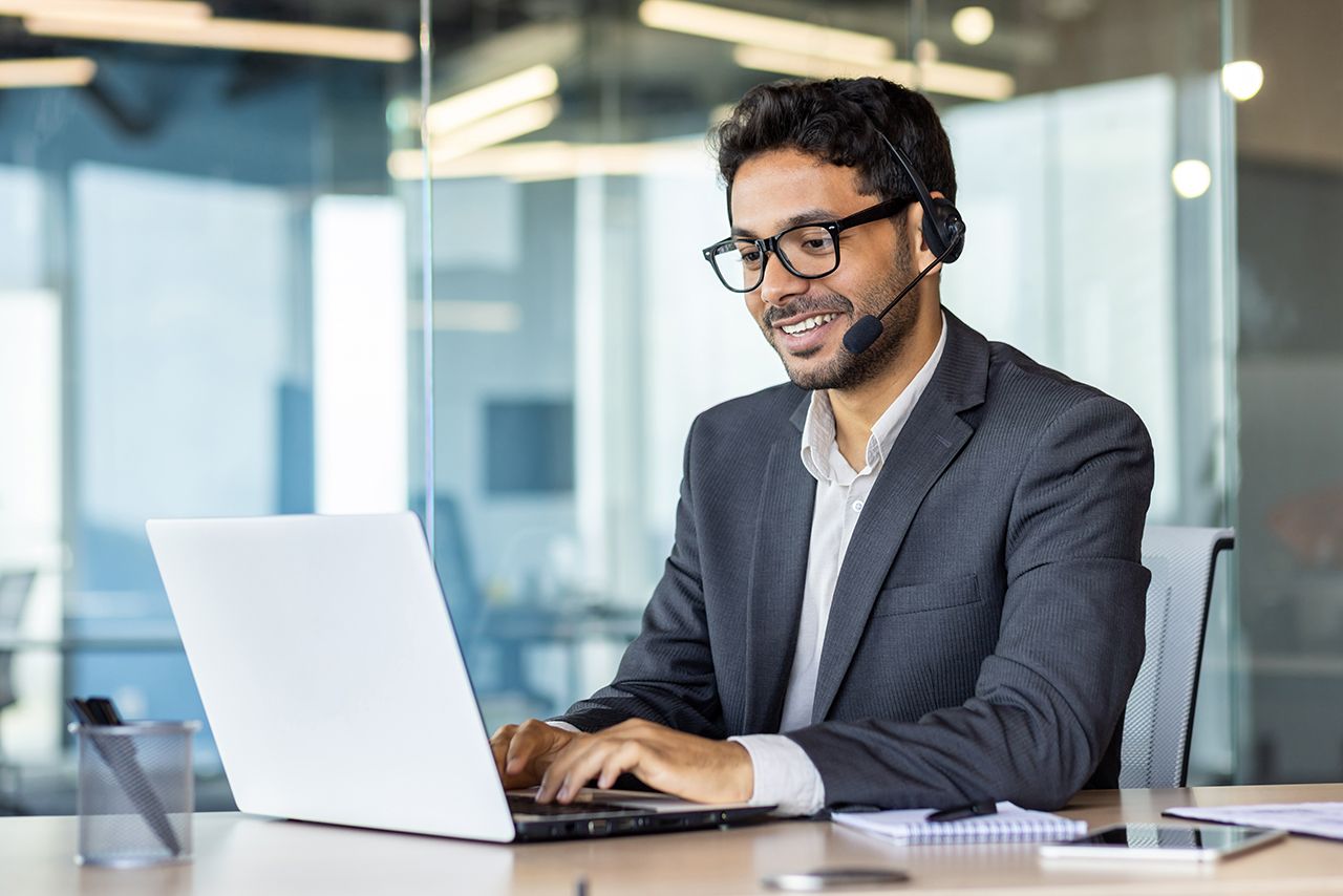 Young man in a business suit wearing a headset and working on a laptop