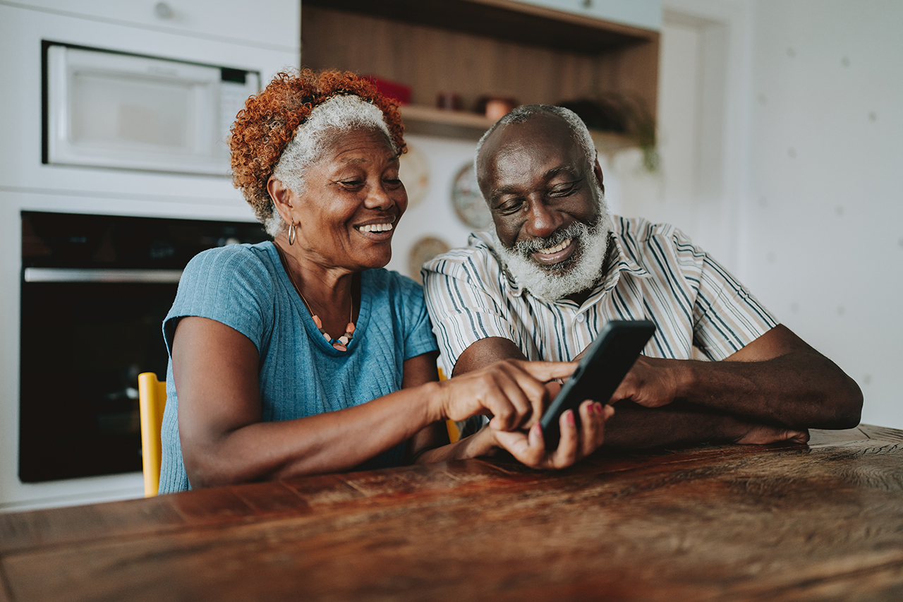 Older couple sitting together, smiling, and looking at a smartphone