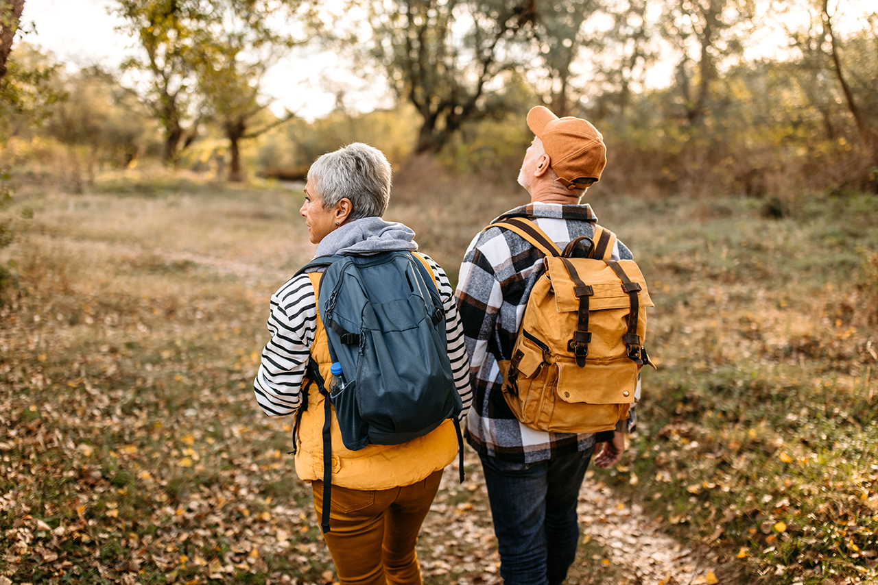 Elderly couple walking through a forested area with backpacks