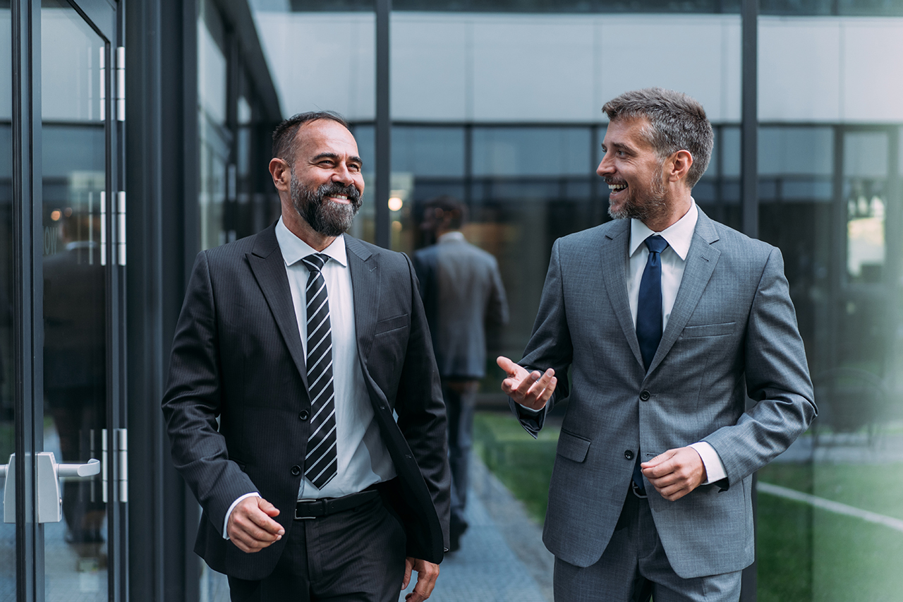 Businessman smiling while walking outside, holding coffee and looking confident