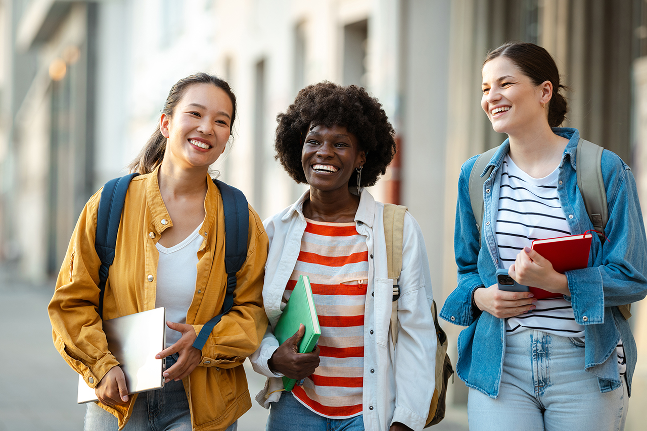 Three women walking together down a city street, chatting and smiling