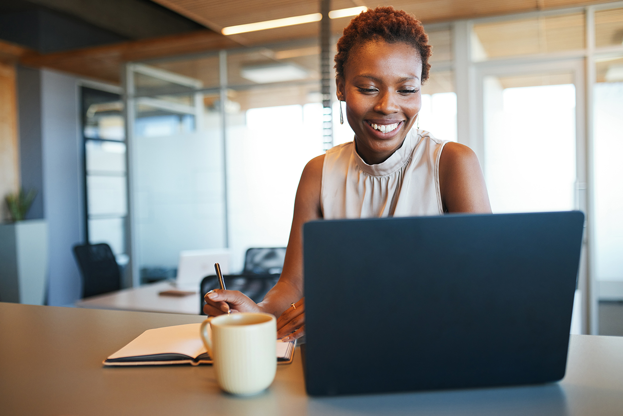 Woman working on a laptop at a desk with a cup of coffee in a modern office