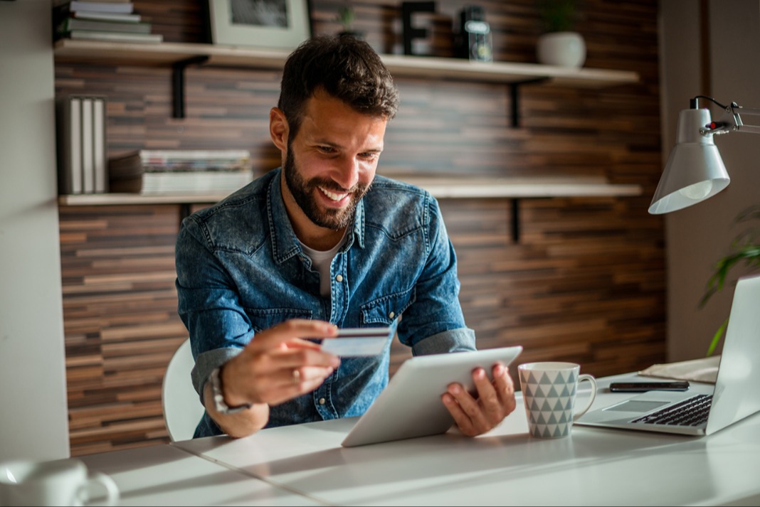 Man sitting at a desk, smiling while looking at a tablet