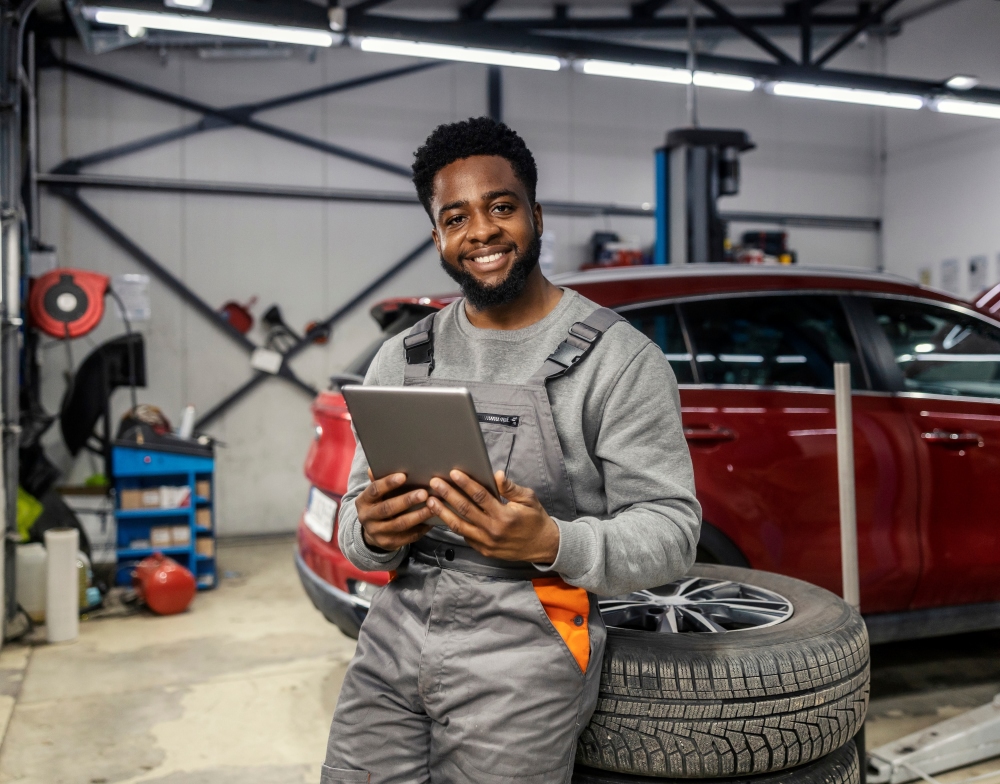 Car mechanic in his shop leaning on tires and holding an ipad.