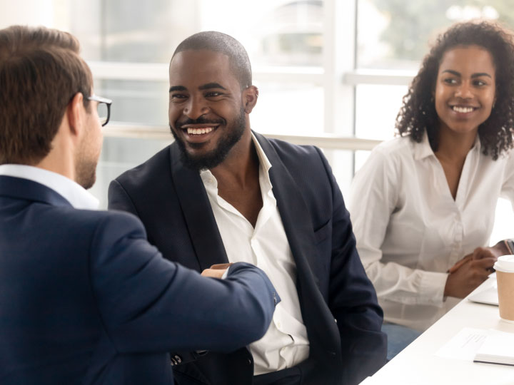 young African American couple in business attire talking to white man in business attire shaking hands