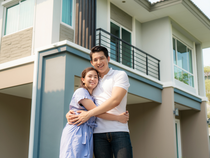 young Asian couple hugging in front of their new home. 